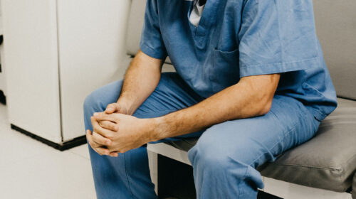 Ein männlicher Arzt sitzt auf einer Wartezimmerbank.