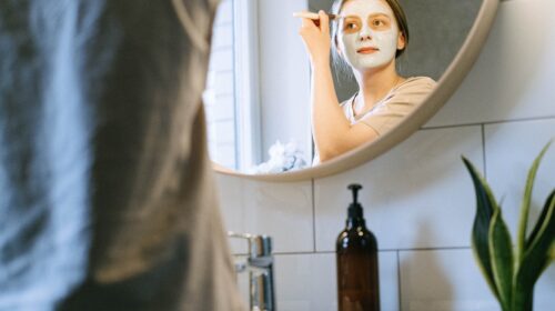 Eine Frau trägt sich vor einem Spiegel eine Gesichtsmaske auf